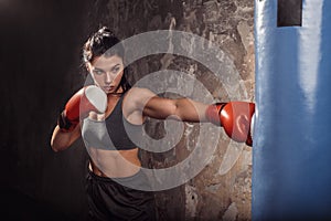 Boxing. Woman boxer in gloves exercise with punching bag practising kick side view
