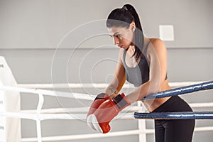 Boxing. Woman in gloves boxer leaning on rope on ring looking down pensive