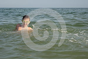 Boy 10 years old in green swimming goggles bathes in the sea