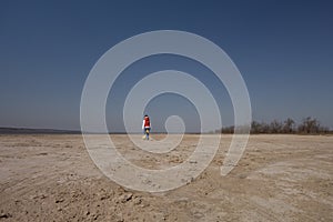 A boy of 10 years old in a white sweatshirt and orange vest plays football on a deserted beach in solitude