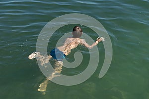 A boy of 11 years old is learning to swim in the blue water of a natural pond