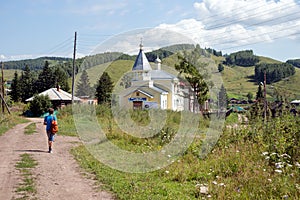 A boy, 12 years old, with a backpack is walking along a dirt road to a church in the village of Parnaya on a summer sunny day.