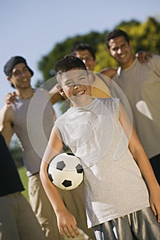 Boy (13-15) holding soccer ball with four men at park.