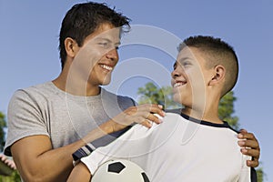 Boy (13-15) holding soccer ball with young man