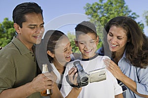 Boy (13-15) looking at camcorder with family outdoors.