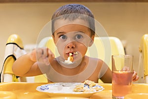 The boy 2 years eats meat. Children`s table. The concept of the child`s independence. Cute toddler boy with spoon is