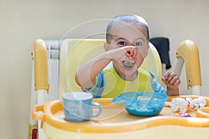 The boy 2 years eats porridge. Children`s table. The concept of the child`s independence. Cute toddler boy with blue