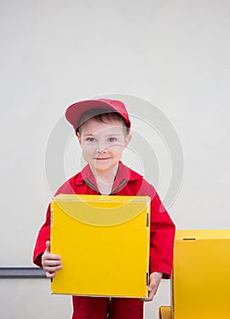 Boy 3-4 years old in a red uniform and cap with a yellow cardboard box in his hands