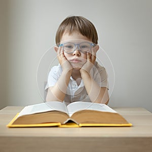 boy 3 years old sits at a desk and is bored in front of an open book, dyslexia concept, boring school