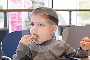 A boy of 4 years old eats nuggets with sauce in a fast food cafe.