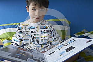 Boy (5-6) sitting in bed reading book portrait