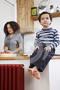 Boy (5-6) sitting on kitchen counter mother in backbround