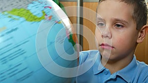 A boy of 6-7 years old examines a globe. Teaching children at school. Children and Geography.