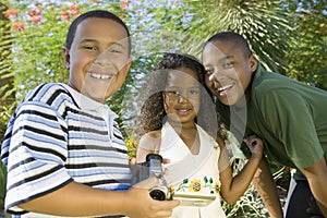 Boy (7-9) holding camcorder with younger sister (5-6) and older brother (10-12) portrait.