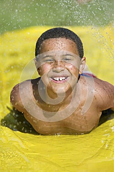 Boy (7-9) sliding on water slide front view portrait.