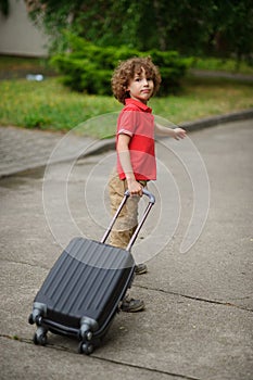 The boy of 8-9 years drags a big suitcase on castors.