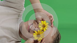 Boy of 9 years covered his eyes with yellow daisies. Closeup