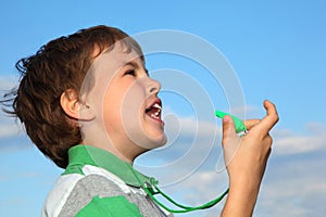 Boy, against blue sky, plays with whistle