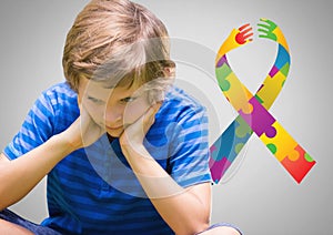 Boy against grey background with autism color spectrum hands ribbon