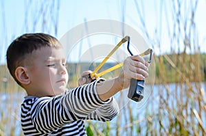 Boy Aiming Sling Shot Outdoors by Lake