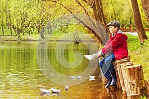Boy alone near pond playing with paper boats