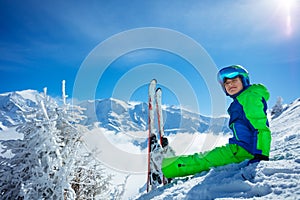 Boy with alpine ski sit in snow over mountain peaks and clouds
