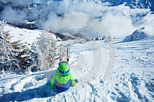 Boy with alpine ski sit in snow on top of steep mountain slope