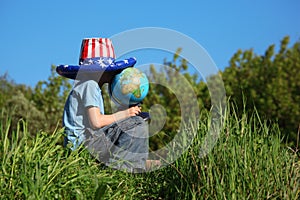 Boy in american flag hat sits and holds globe