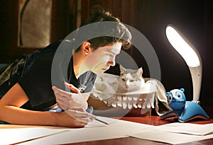 Boy architect student working on drafting project in night with cat in box beside