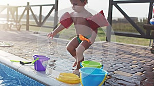 Boy with armbands playing with toys near the pool with clear water on the background of a summer sunset