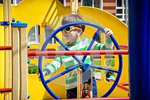 Boy as a captain or sailors play on the ship outdoors on sunny day. Kid has a lot of fun. Ship has colorful flags on wind