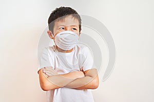 A boy of Asian appearance stands in a white medical mask, folded his arms over his chest - the child on a white background looks