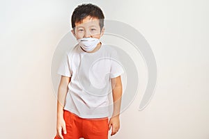 A boy of Asian appearance stands in a white medical mask, improperly dressed the mask - the child on a white background shows that