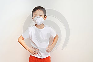 A boy of Asian appearance stands in a white medical mask, put his hands on his side - a child on a white background