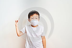 A boy of Asian appearance stands in a white medical mask, raised his index finger up - a child on a white background shows that he