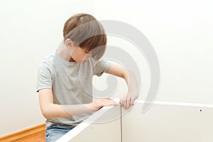 Boy assembles a bookshelf hisself. Son helping his dad to assembling new furniture at home