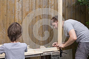 Boy assisting his father in DIY activities in the backyard of countryhouse