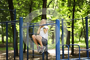 The boy athlete in the park pulls himself up on the horizontal bar grimaced and pulls himself up with effort