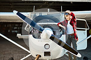 Boy in aviator glasses stands beside small white propeller airplane