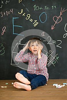 A boy on the background of a blackboard solves a difficult task. Sits with crayons and scratches his head