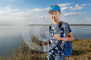 Boy with a backpack on the background of the reservoir, in his hand a bottle of water, a walk through the woods