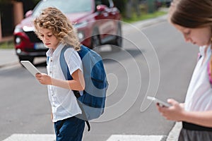 Boy with a backpack, and cellphone goes through the pedestrian crossing, not looking at red cars let him through