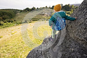 Boy with backpack climbing big stone in hill. Pidkamin, Ukraine