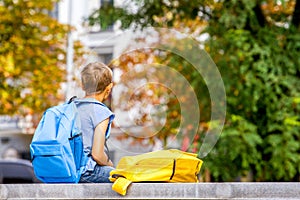 Boy with backpack sitting outdoors after school