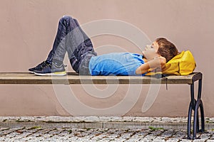 Boy with backpack under head lying on the bench outdoors