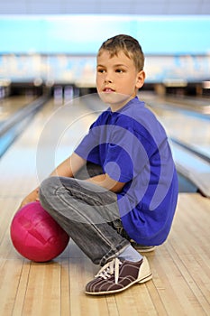 Boy with ball sits on floor in bowling