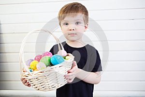 Boy with a basket with Easter eggs on a background of a white wall