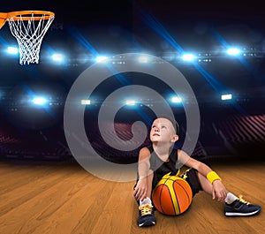 Boy basketball player with a ball sitting on the floor in the gym and dreams of great victories.