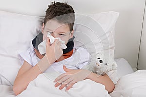 The boy is in bed, his throat hurts, he blows his nose into a paper disposable handkerchief