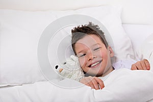 Boy in bed under a blanket with toy smiling